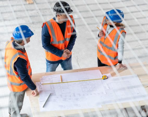 Three construction workers standing studying technical drawings. Photo. 