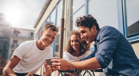 Bilde av tre unge mennesker som ser på en mobil og smiler