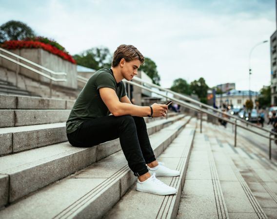 Boy sits outside on the stairs and looks at his mobile phone