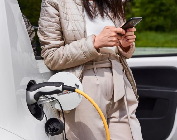 Image of a woman charging an electric car while checking her mobile phone