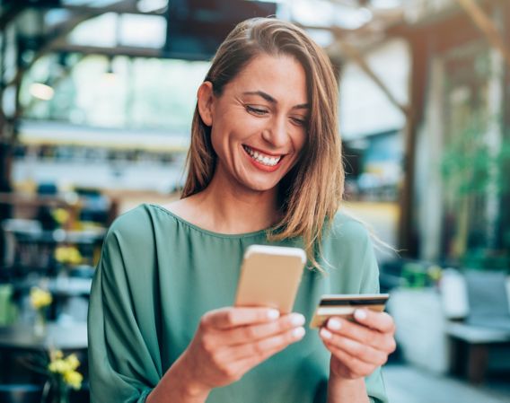 Woman who is smiling while she’s holding a phone and debit card