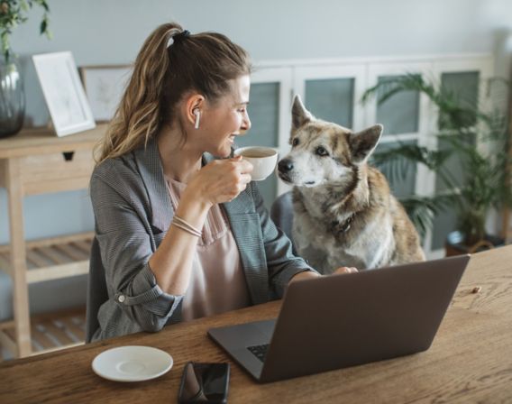 Image of a woman holding a cup of coffee and looking at her dog
