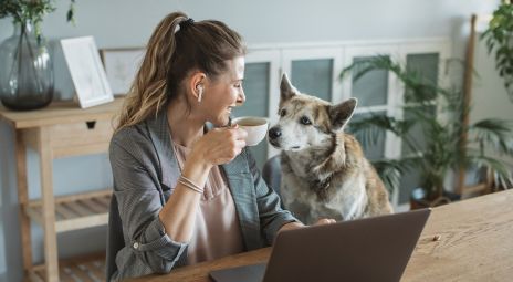 Dame drikker kaffe ved siden av hund og smiler over testvinnende hundeforsikring.
