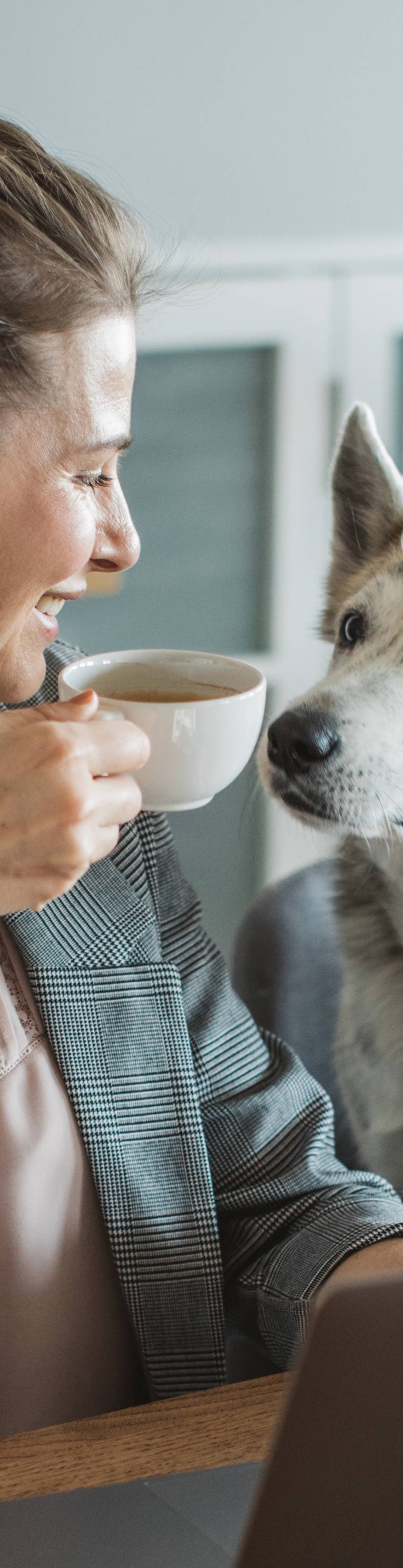 Dame drikker kaffe ved siden av hund og smiler over testvinnende hundeforsikring.