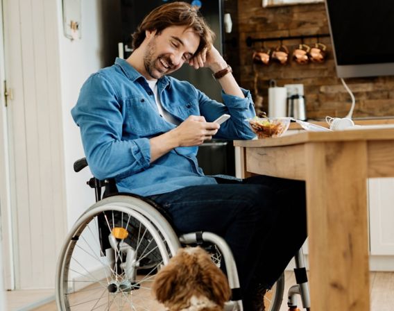 Image of a man sitting in a wheelchair and smiling at his dog