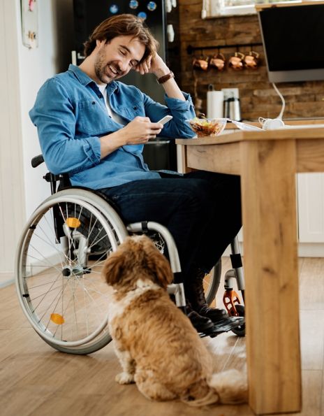 Man in a wheelchair checking his telephone with a dog by his side.