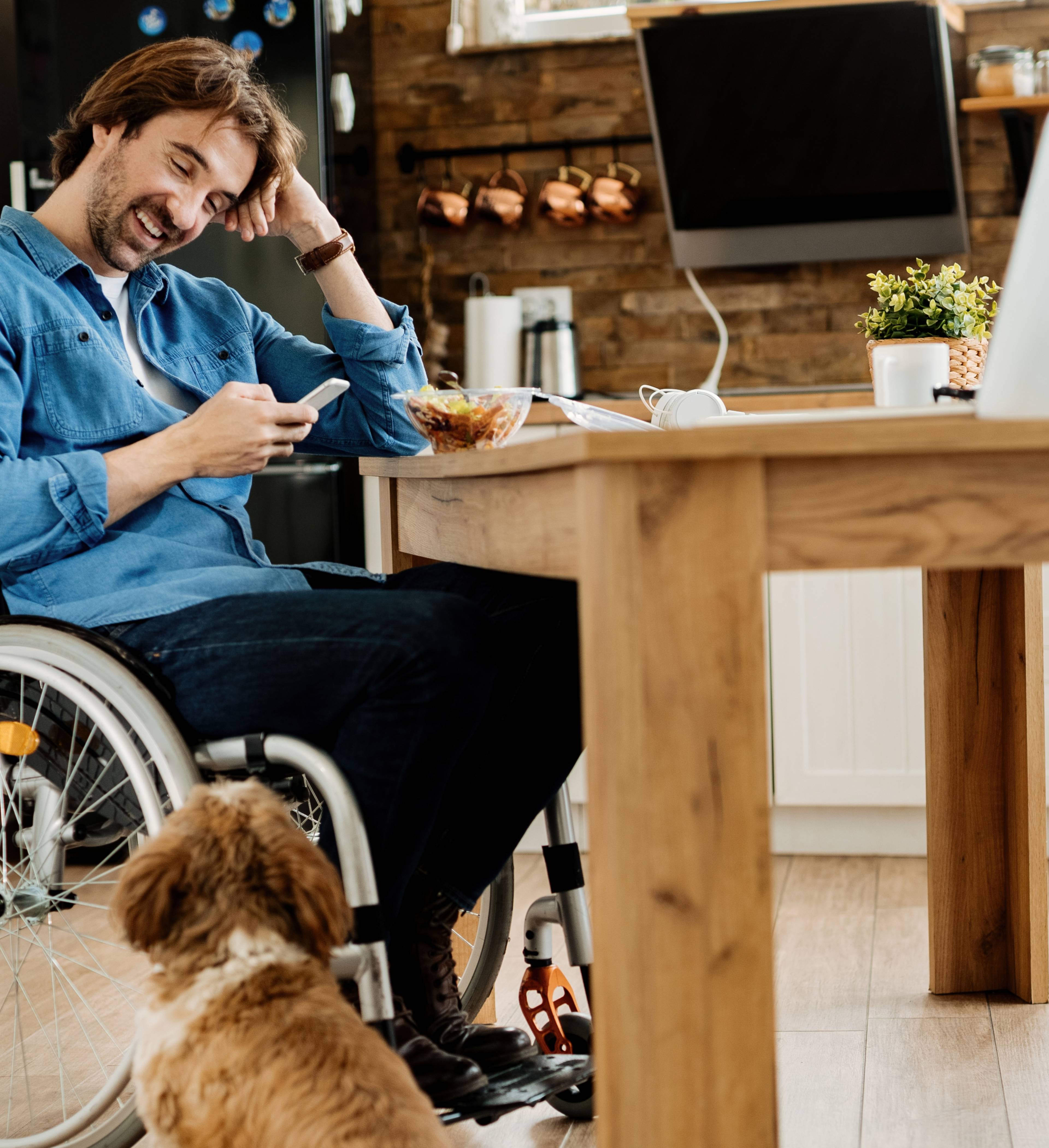 Bilde av mann i rullestol som ser på mobilen med en hund ved siden av seg.