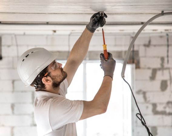 Bilde av en elektrikerinstallatør med et verktøy i hendene, som arbeider med kabel på byggeplassen