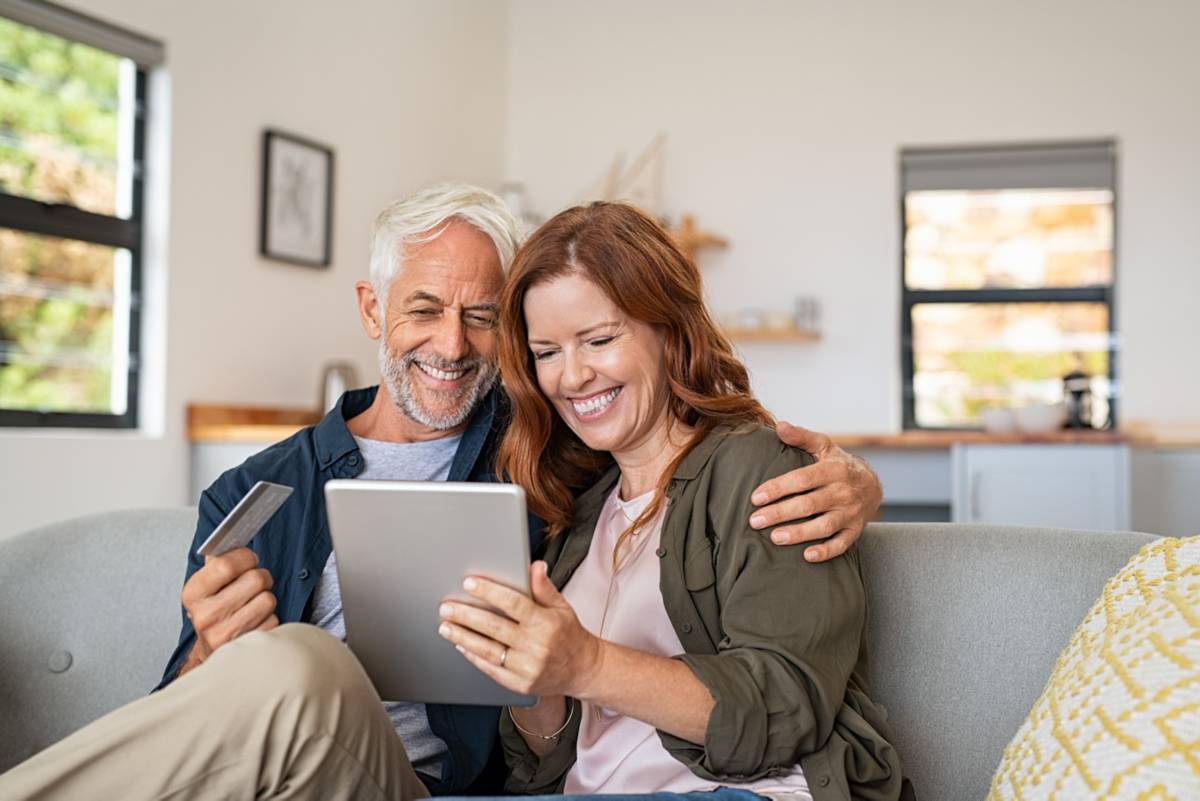 Two people sitting and smiling and tapping on a tablet