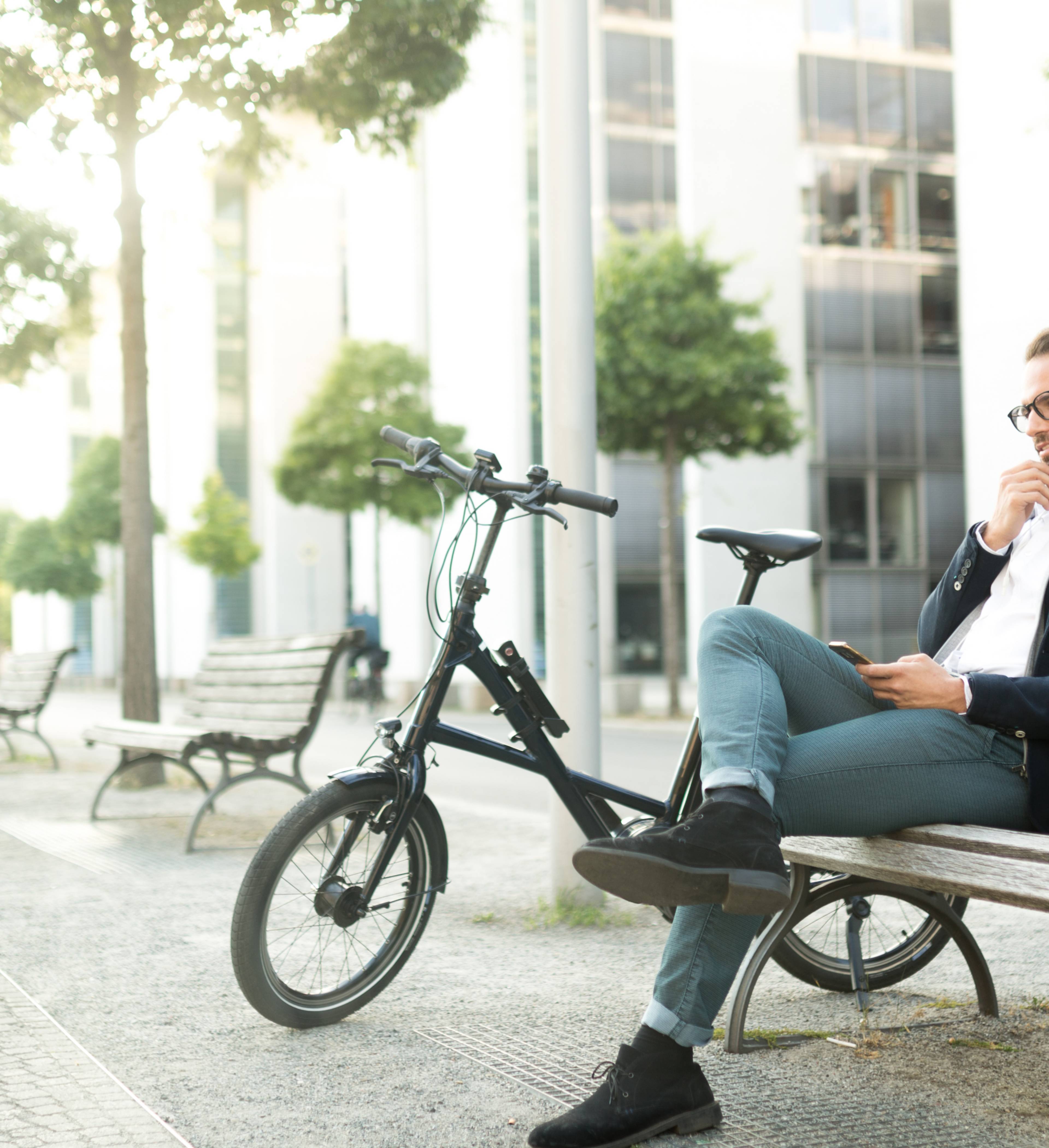 Ung mann med el-sykkel sitter på benk