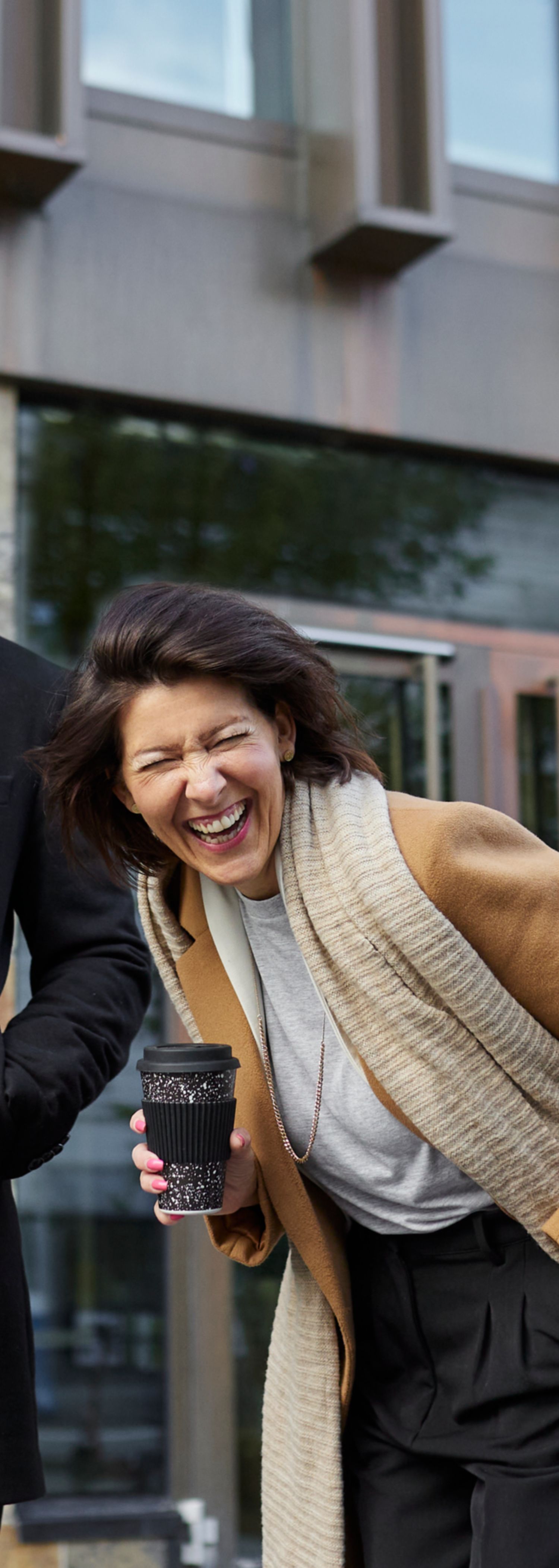 Three colleagues on the street smiling and drinking coffee