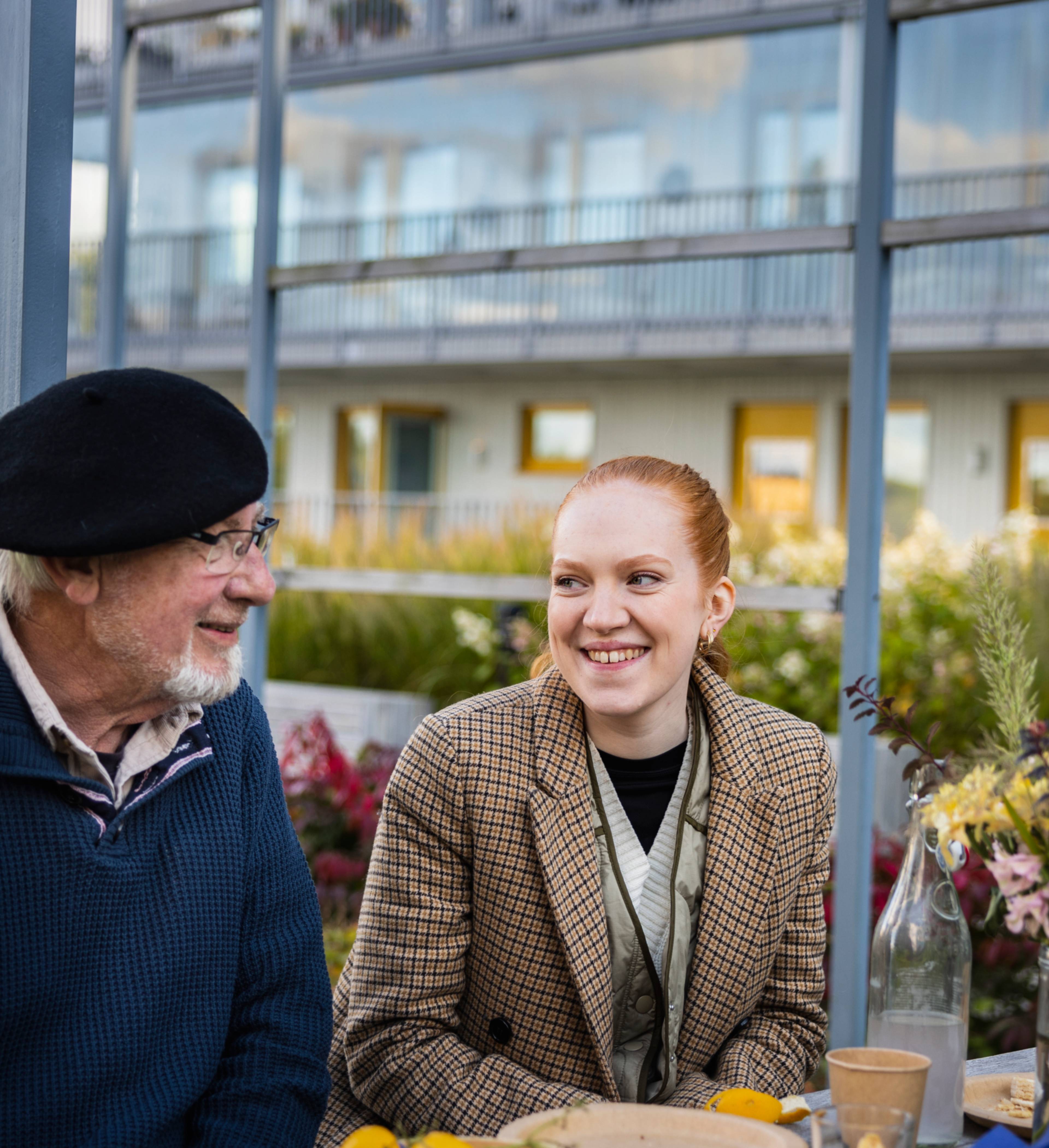 Ung kvinne og eldre mann prater ved et bord i en bakgård