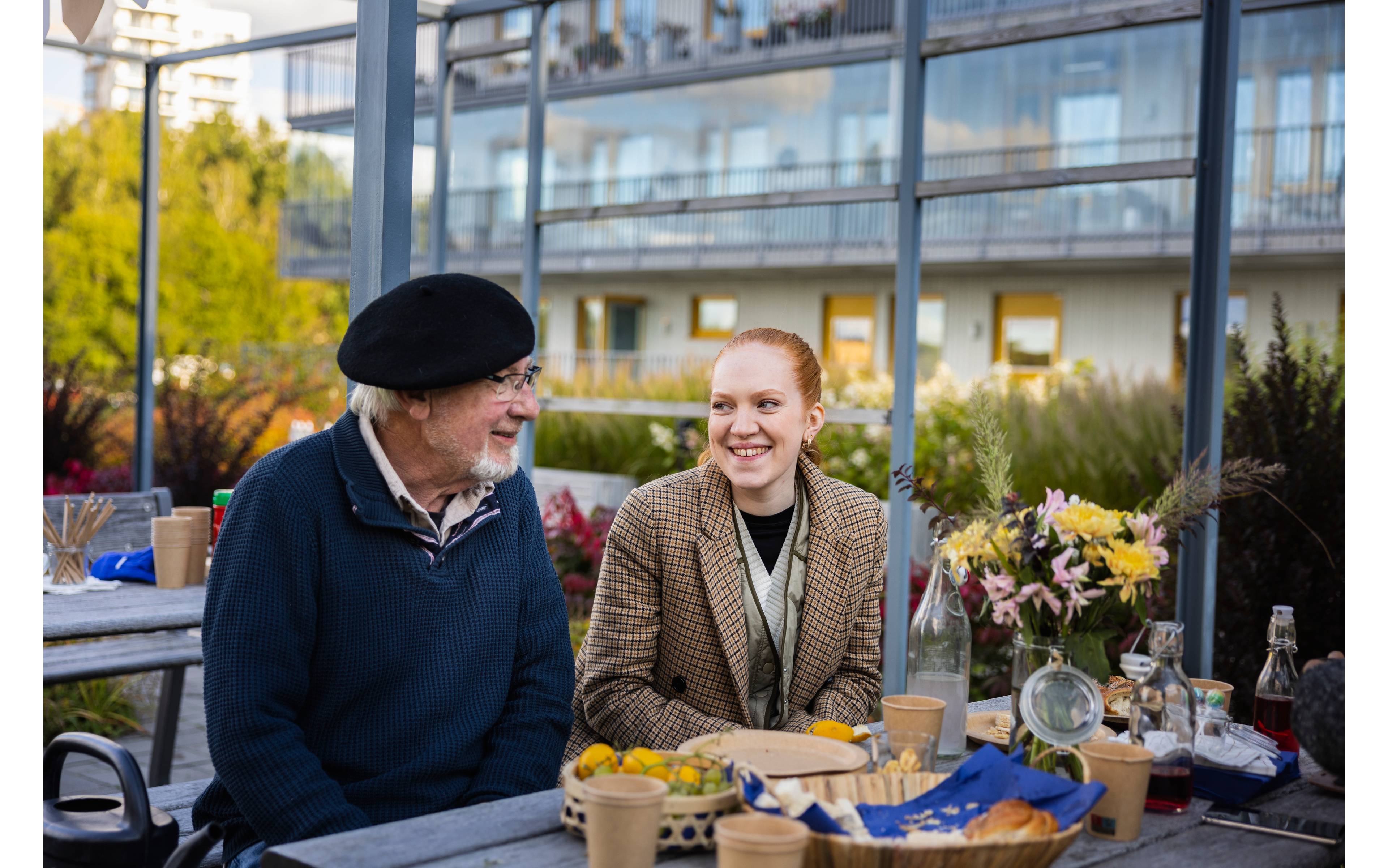 Ung kvinne og eldre mann prater ved et bord i en bakgård