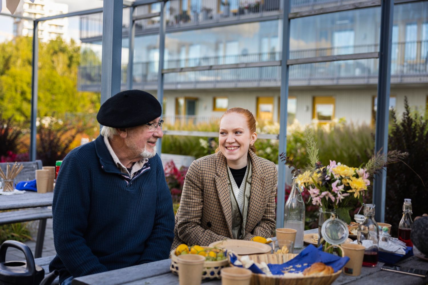 Ung kvinne og eldre mann prater ved et bord i en bakgård