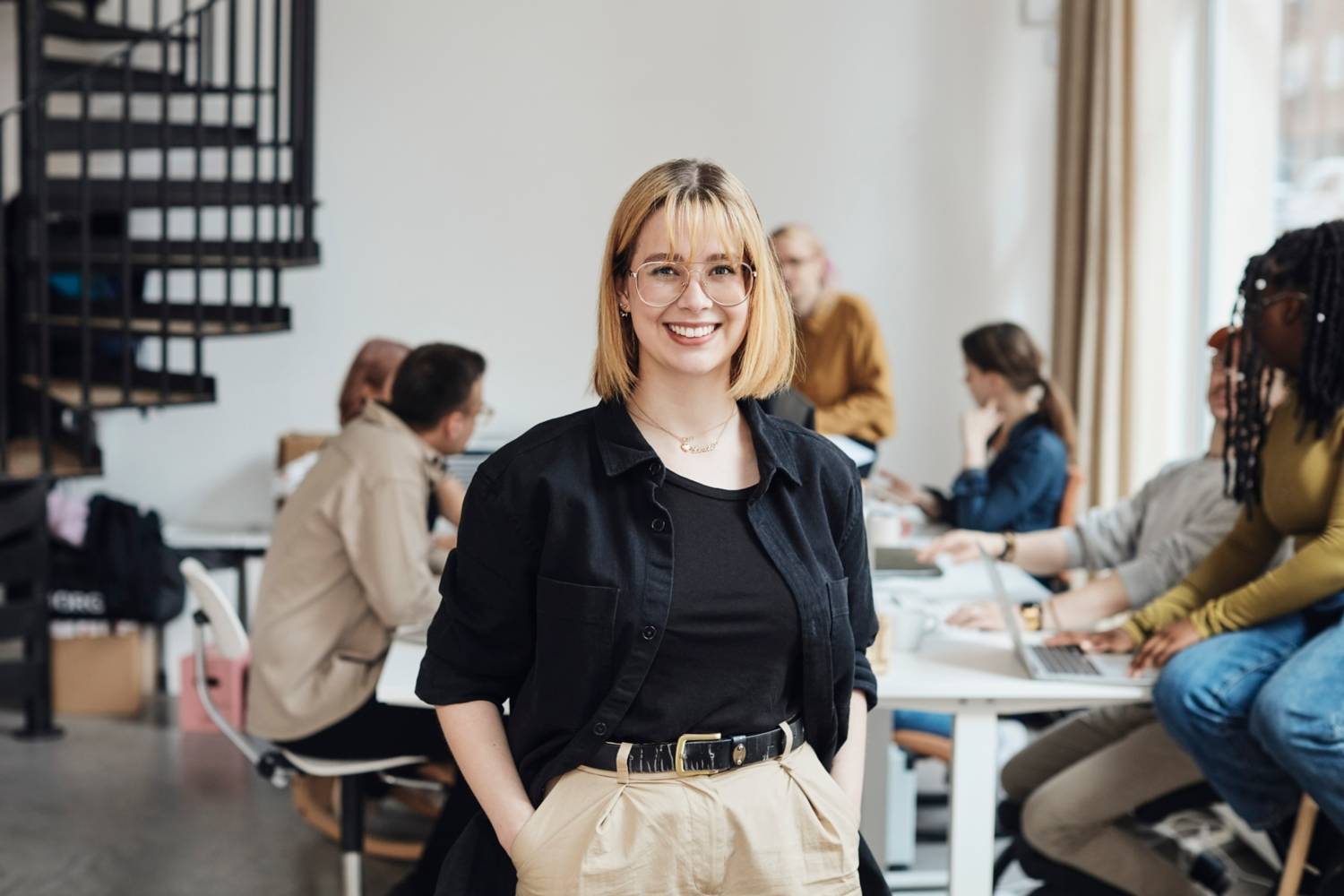Ung kvinne smiler p� kontor med kolleger i bakgrunnen