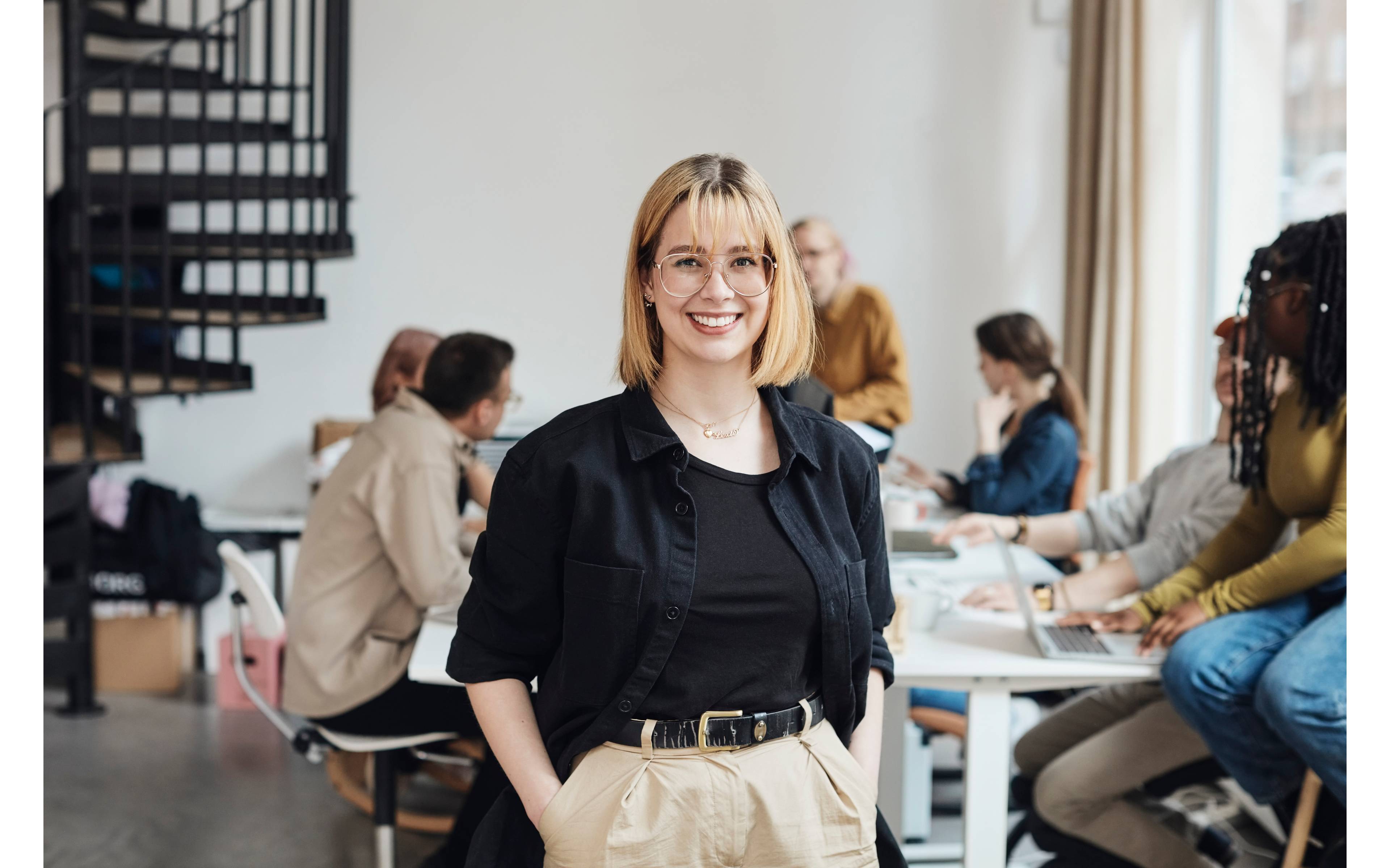 Ung kvinne smiler p� kontor med kolleger i bakgrunnen