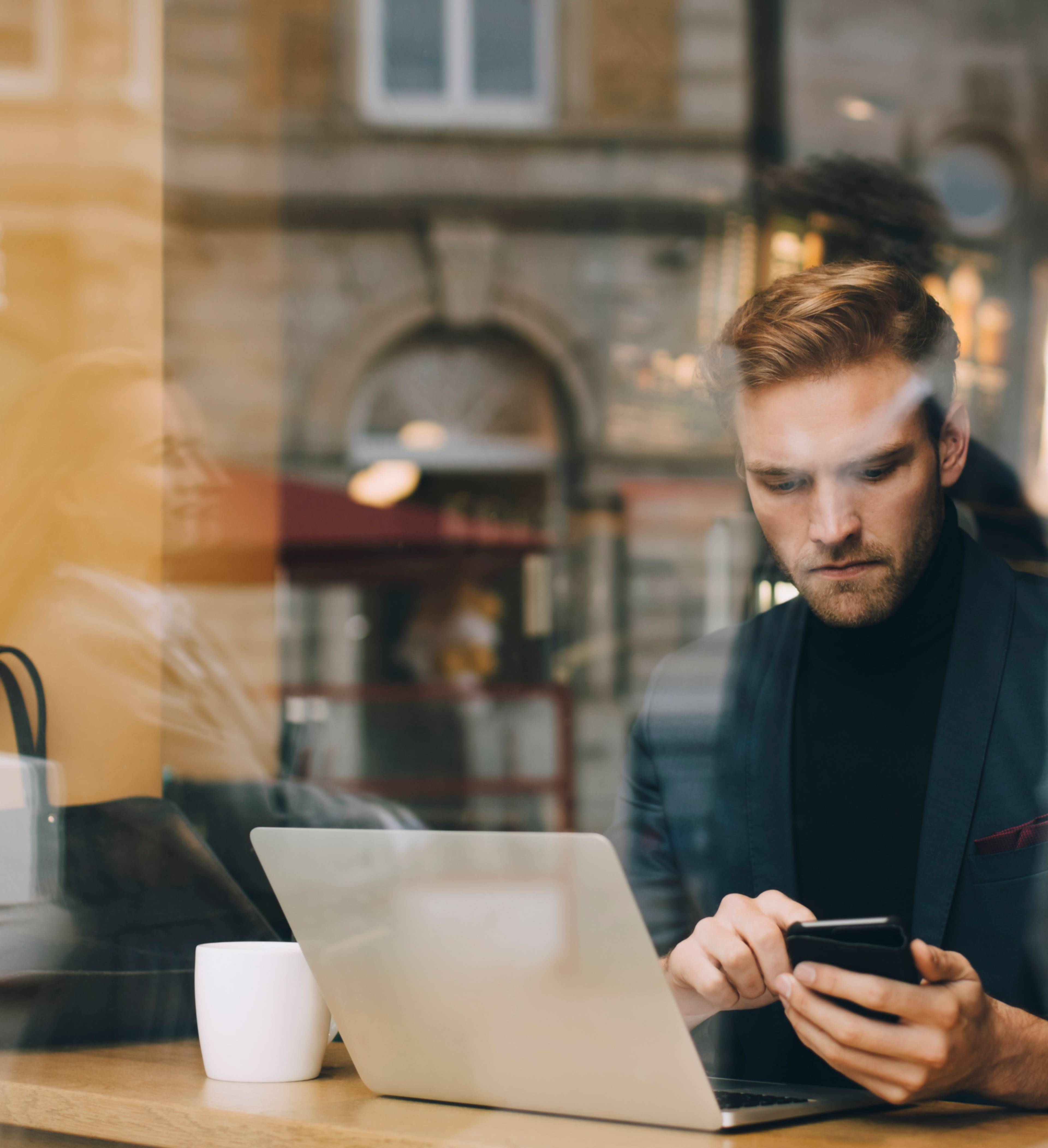 Mann med laptop og telefon på cafe