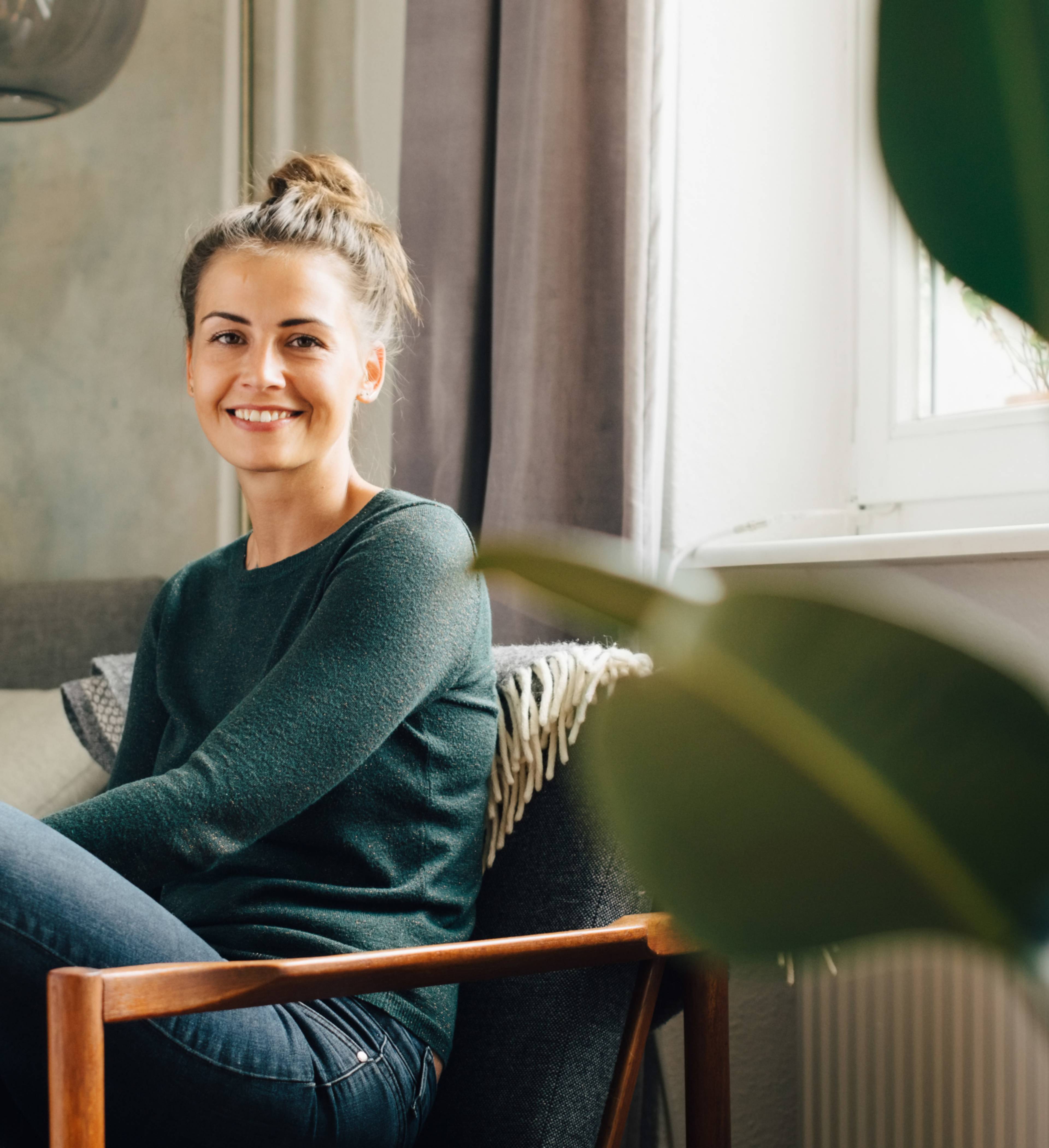 Kvinne sitter i stol hjemme og smiler