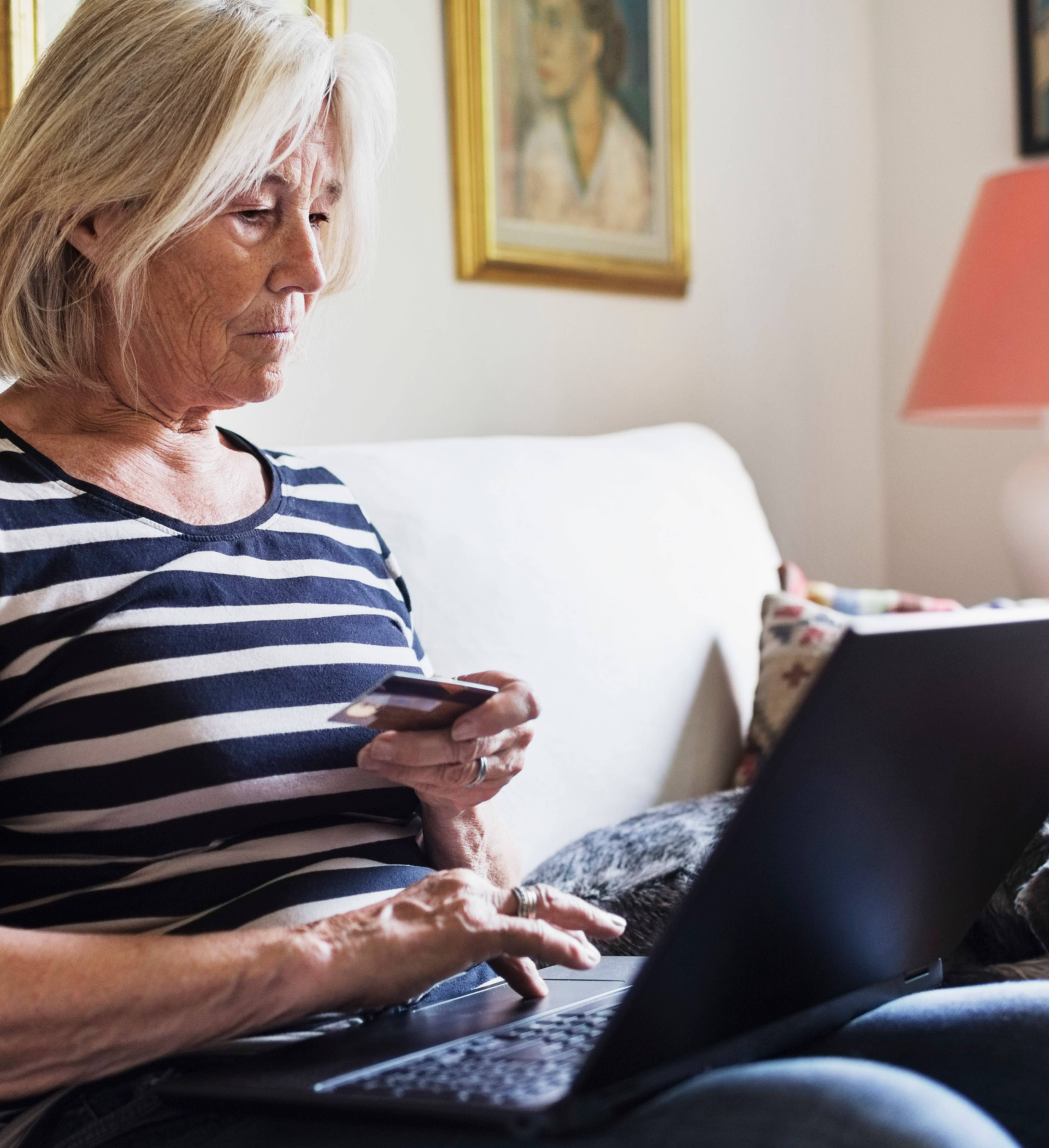 Eldre kvinne holder betalingskort med laptop på fanget