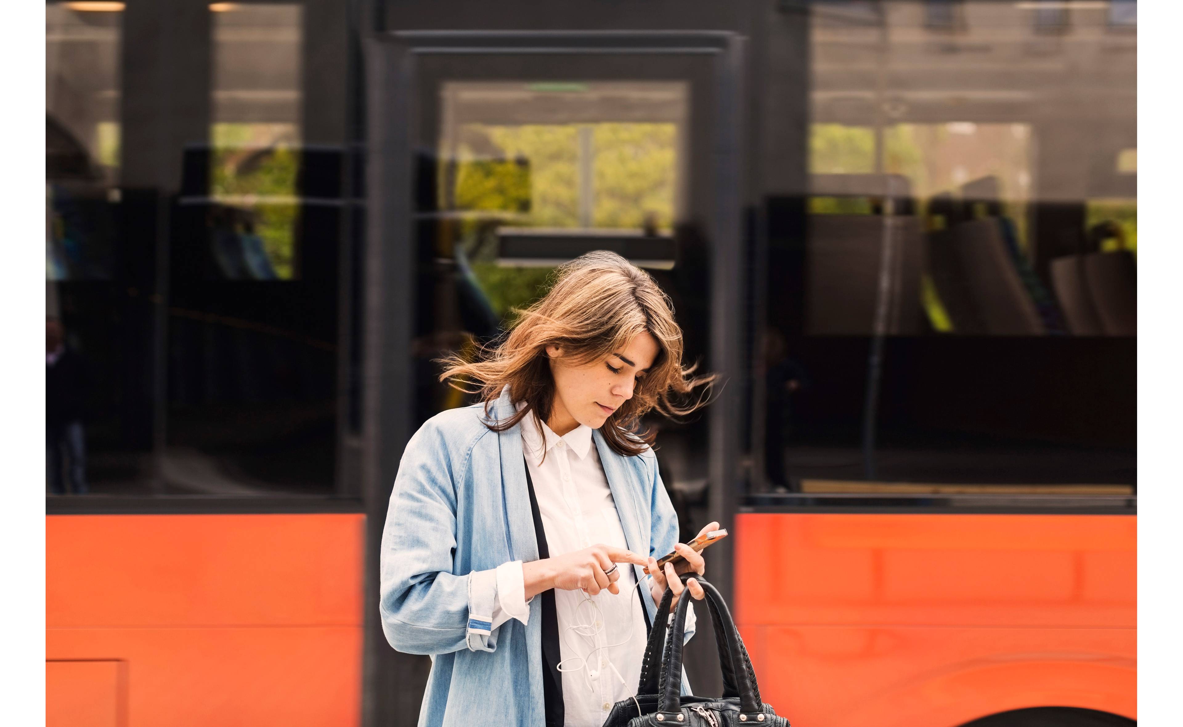Kvinne foran buss trykker på telefonen