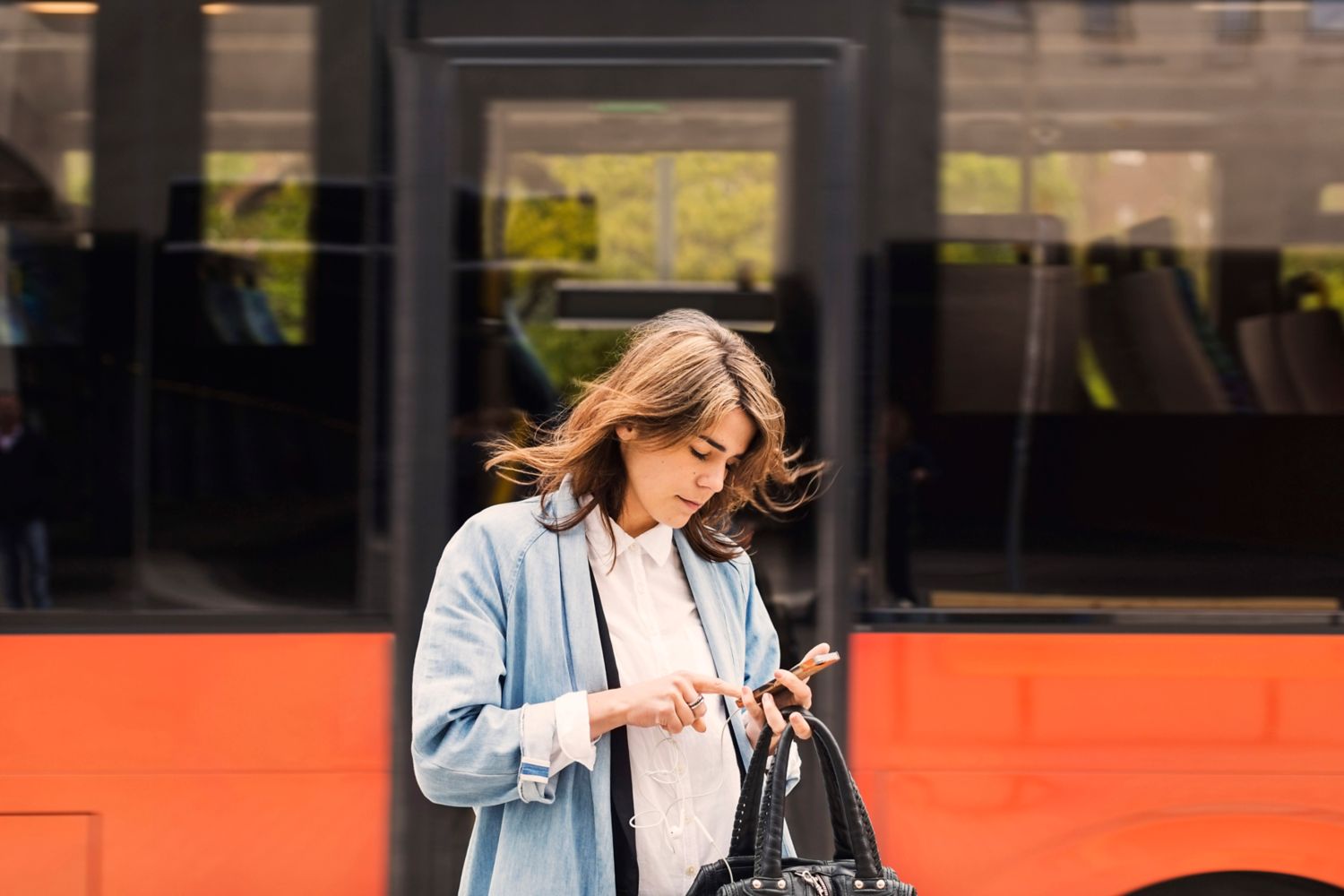 Kvinne foran buss trykker på telefonen