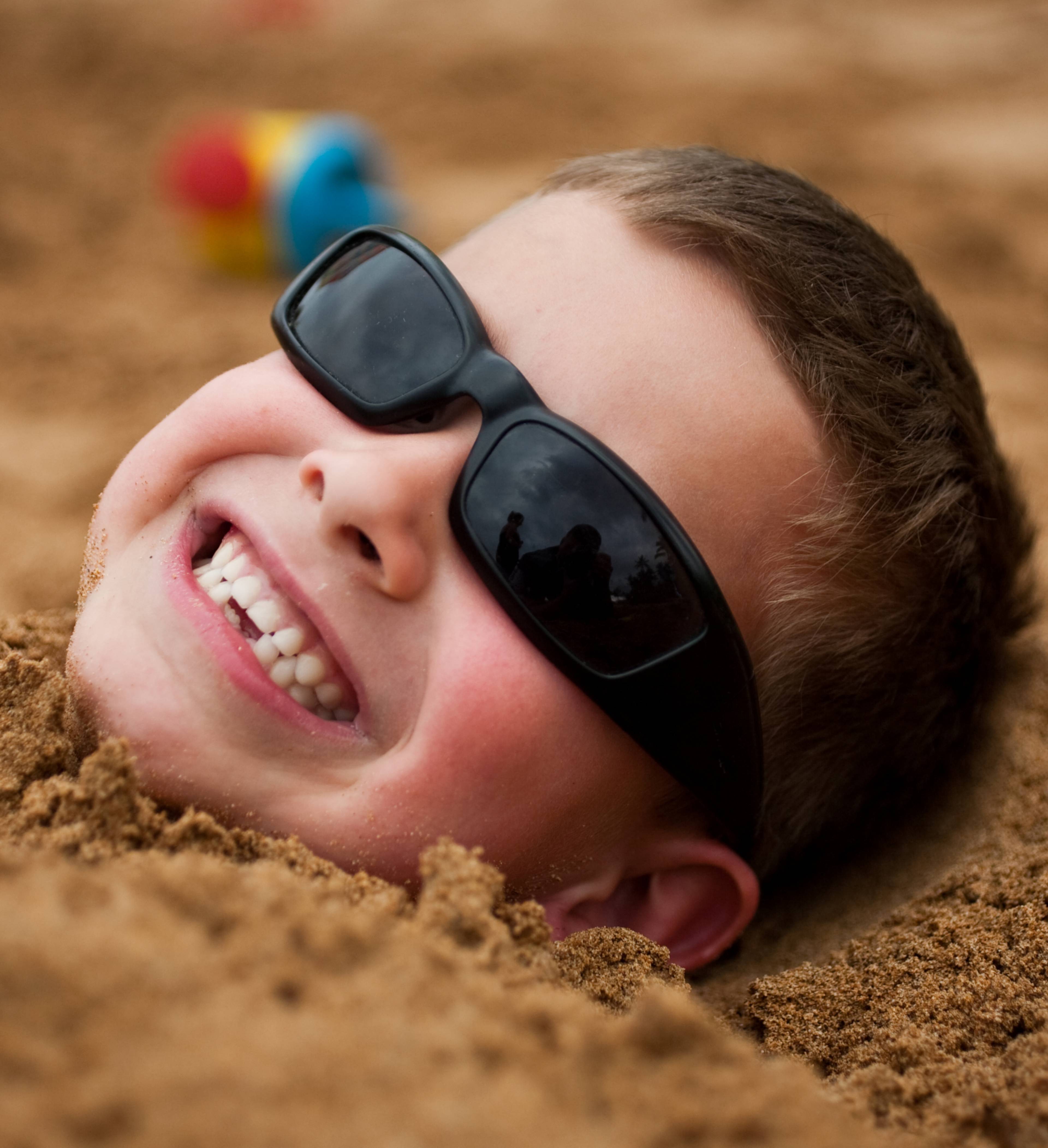A young boy buried in the sand on a beach.
