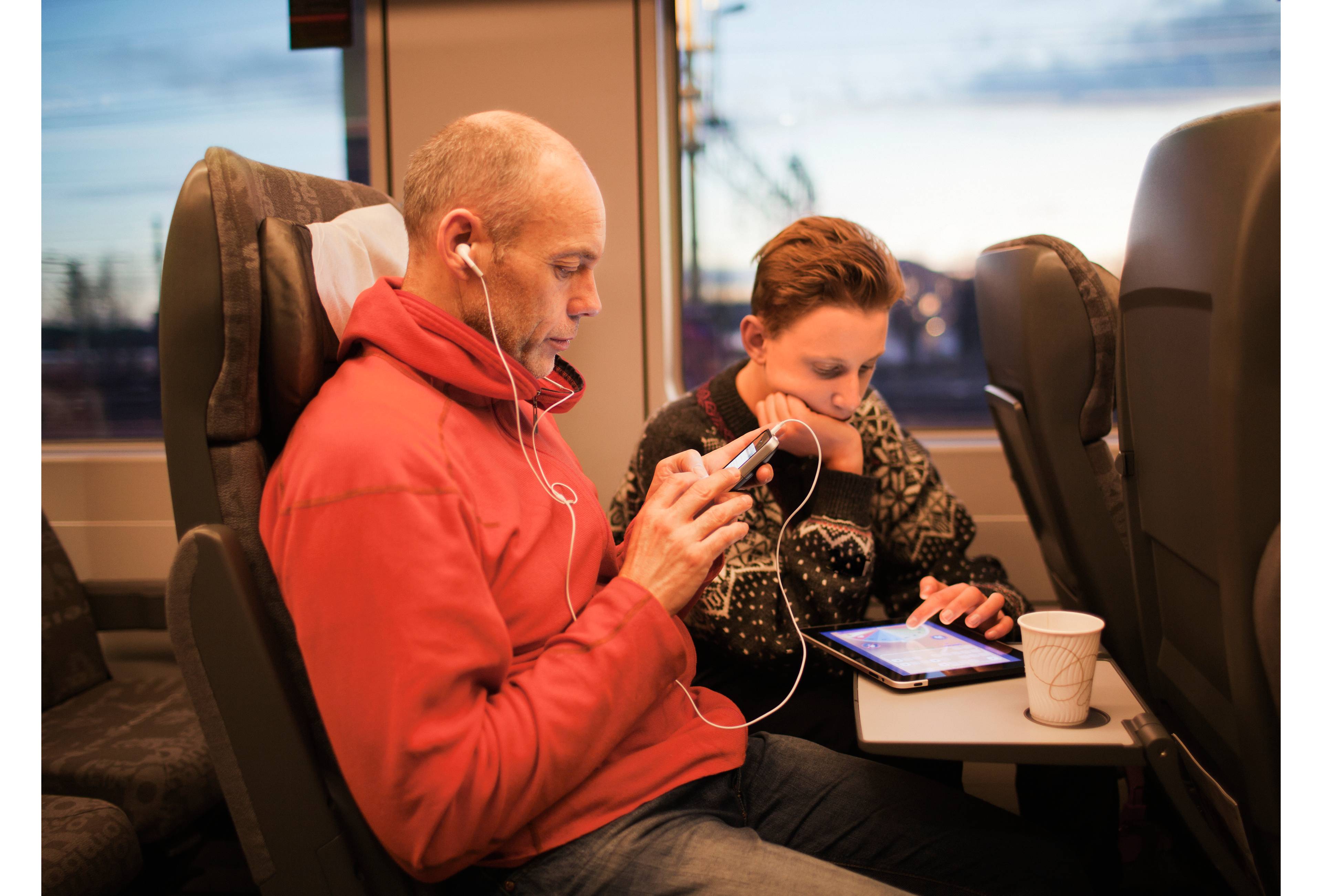 Far og sønn sitter på tog med mobil og nettbrett