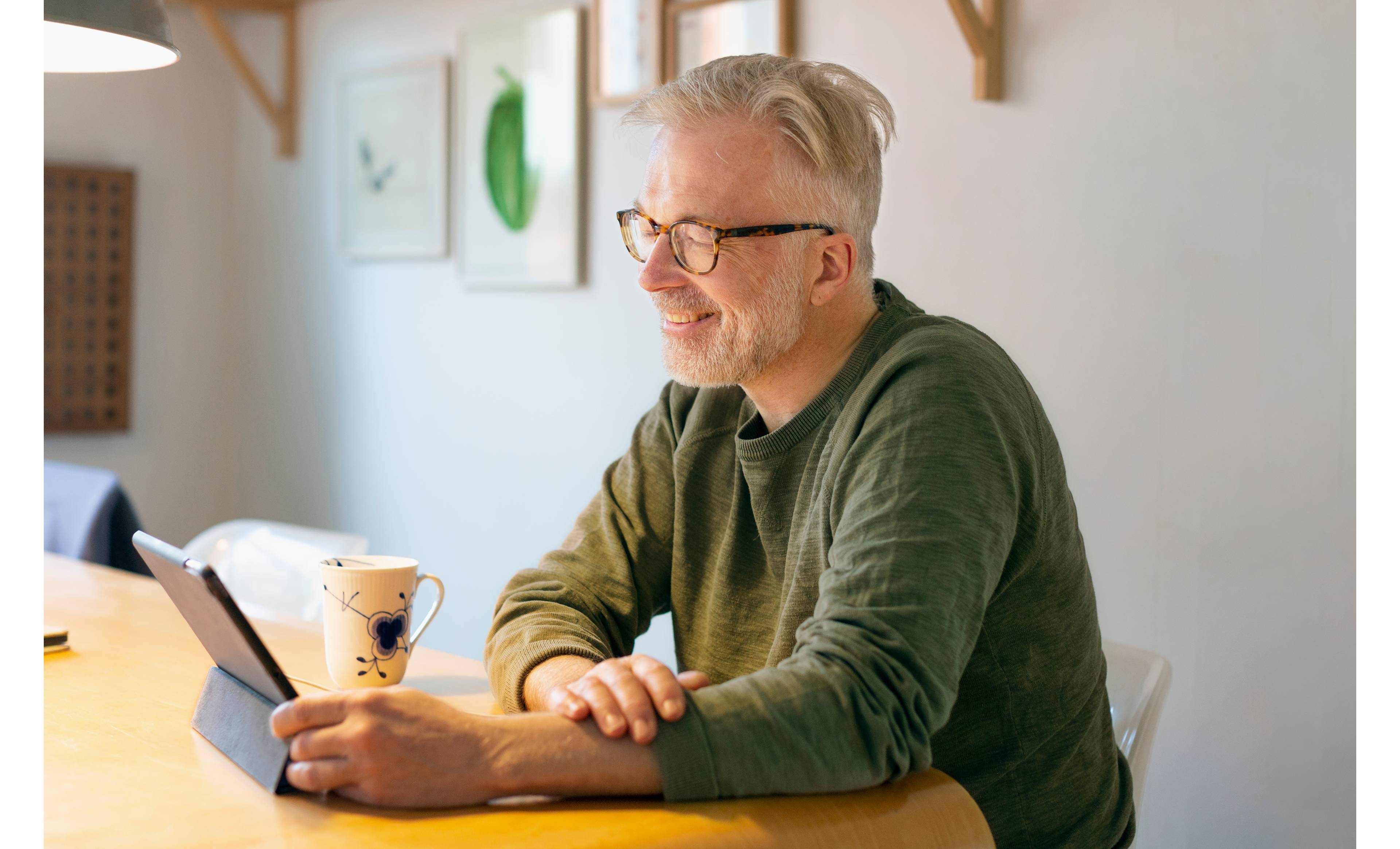 Mann sitter ved spisebordet med nettbrett