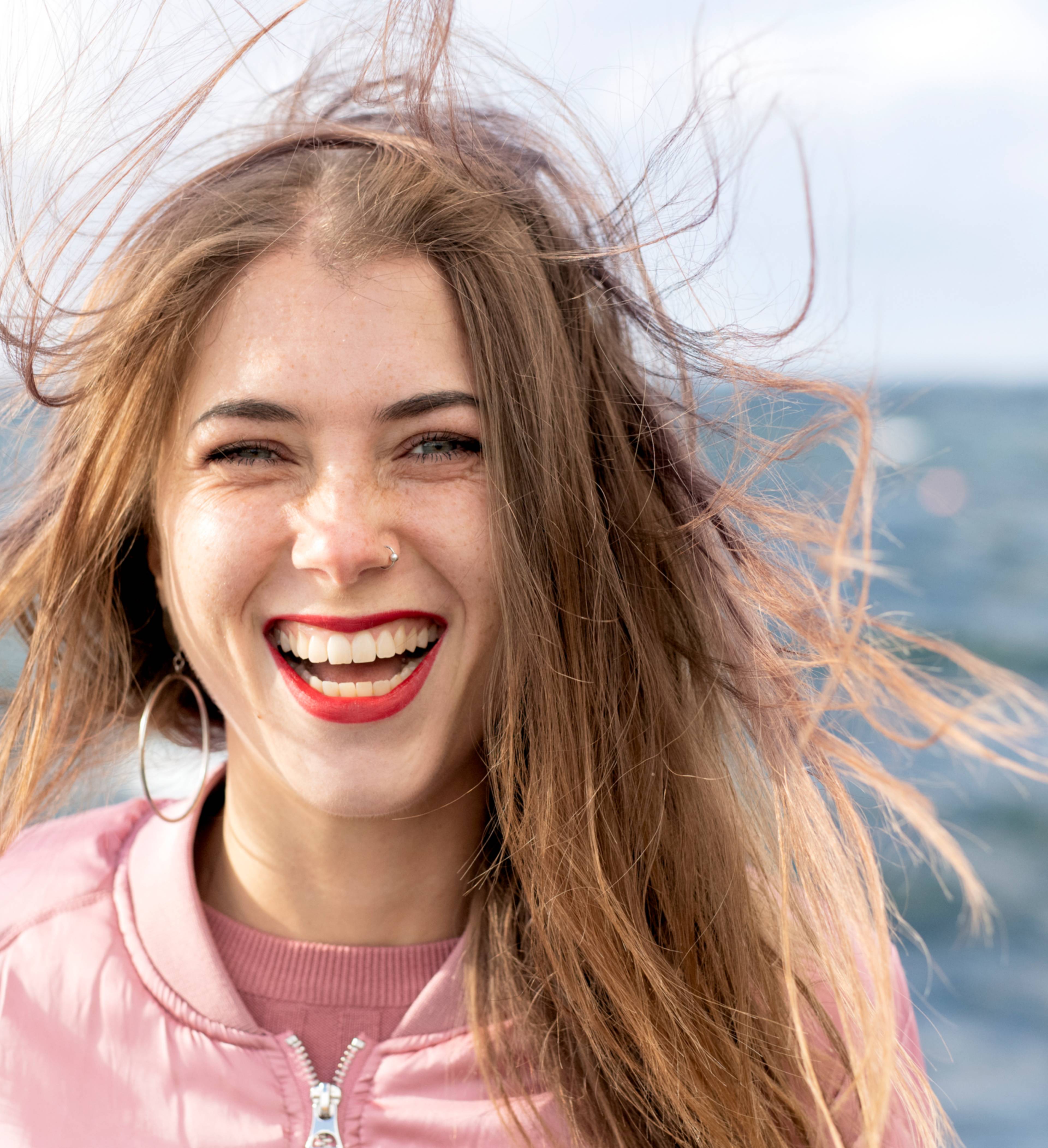 Glad kvinne med vind i håret ved havet