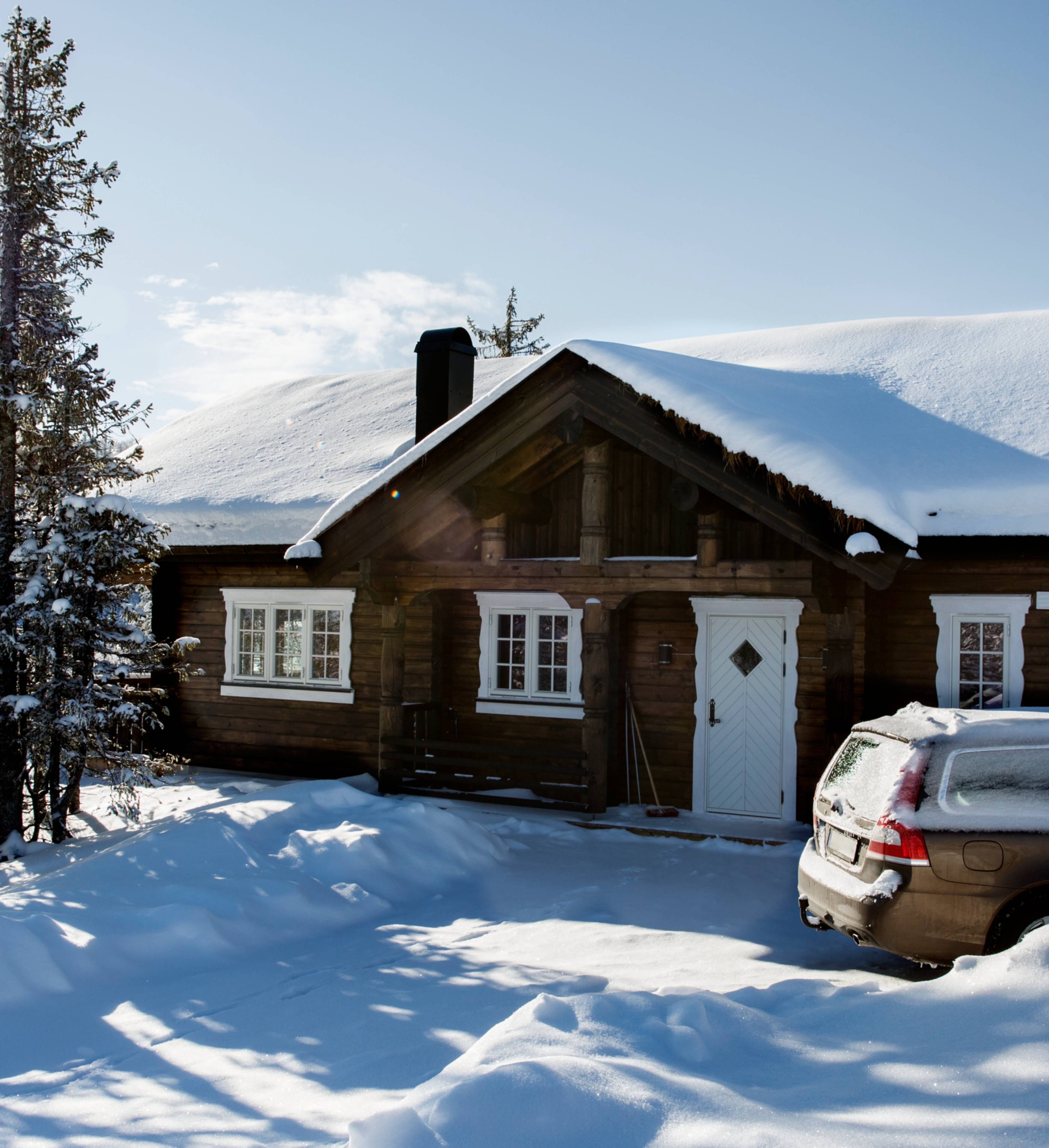 Hytte dekket i snø med bil utenfor