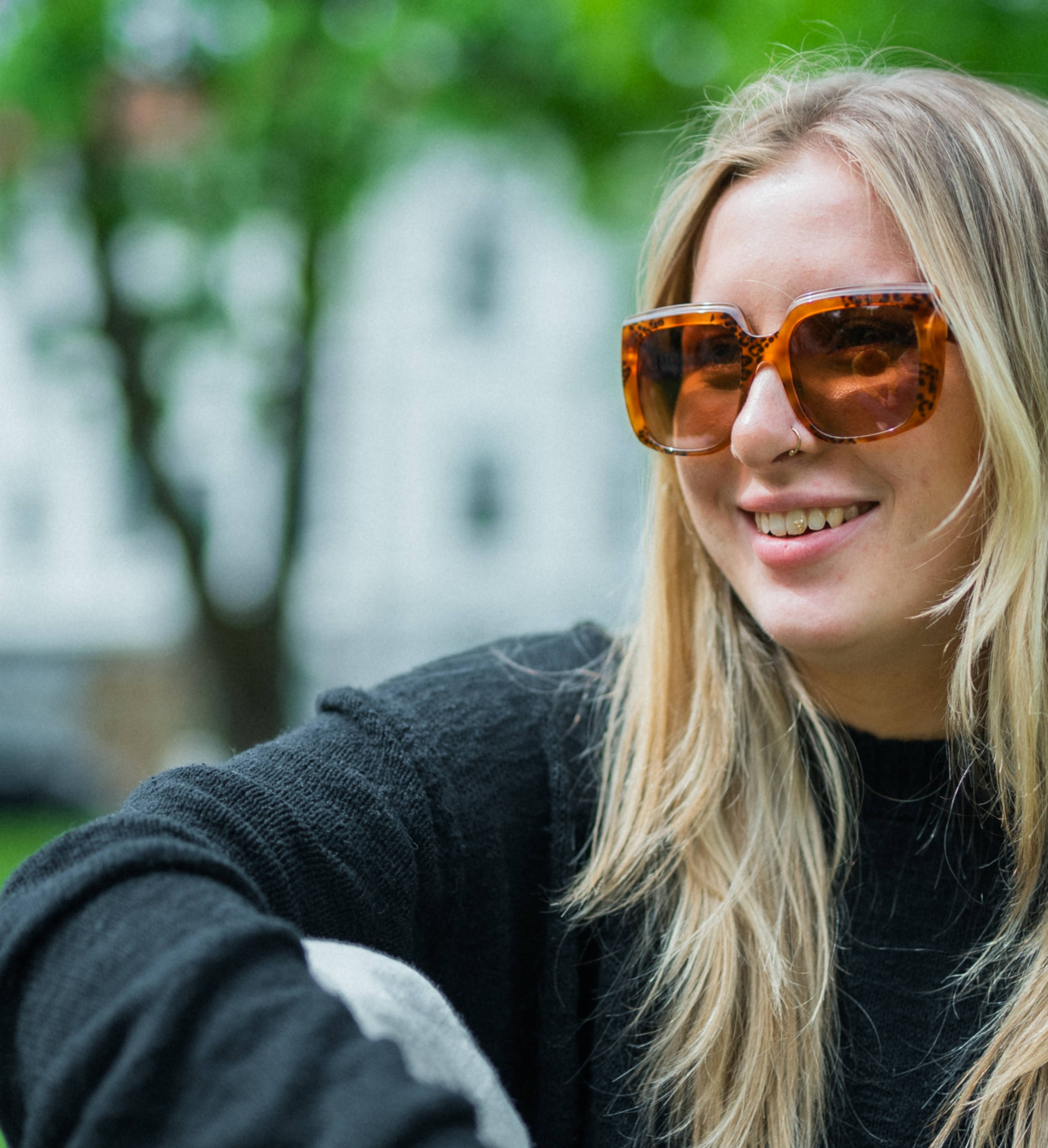 Smilende jente med solbriller i parken