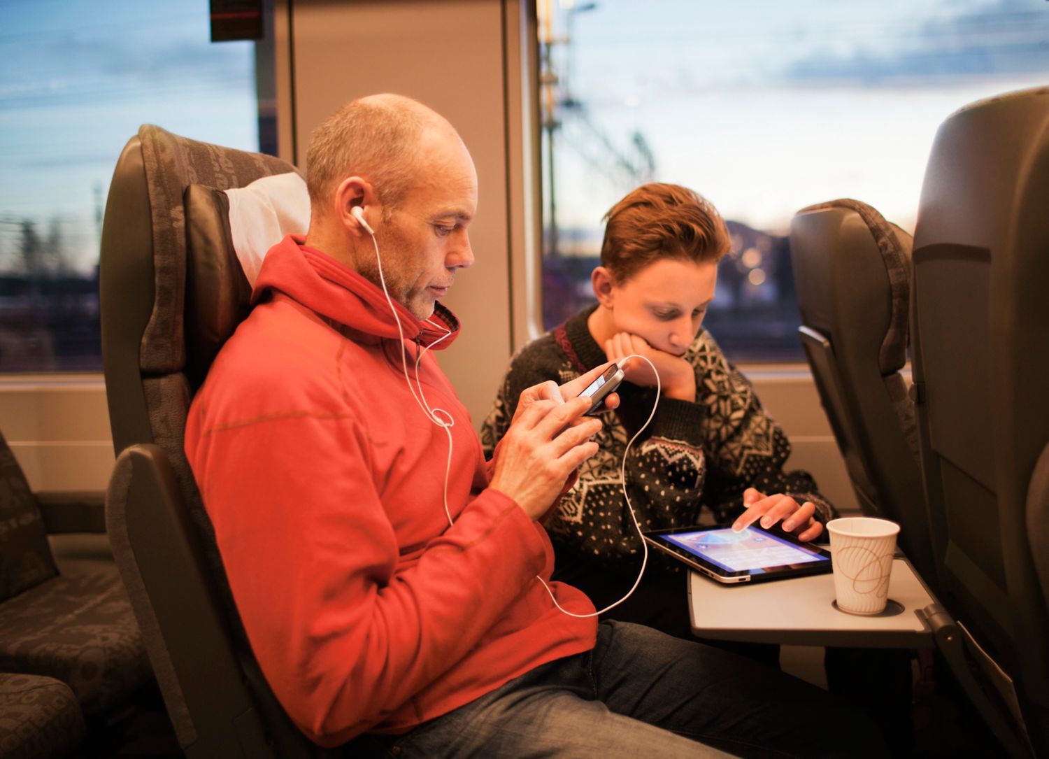 Far og sønn sitter på tog med mobil og nettbrett